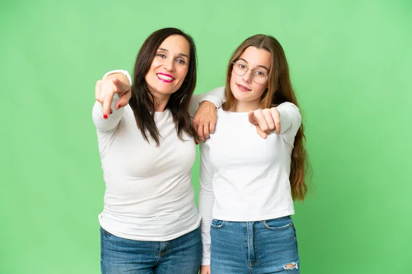 mother and daughter over isolated chroma key background points finger to the front