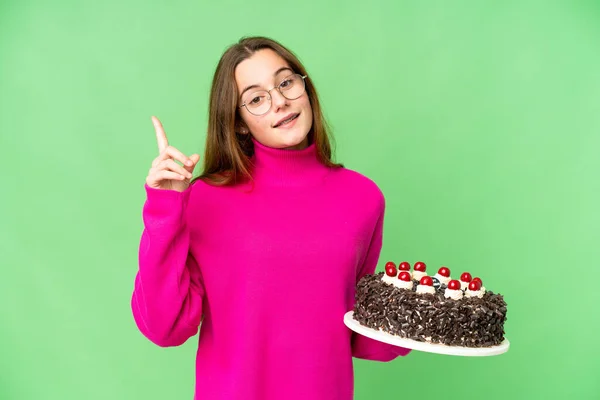 将生日蛋糕放在孤立的彩色背景下的少女指出了一个伟大的想法 — 图库照片