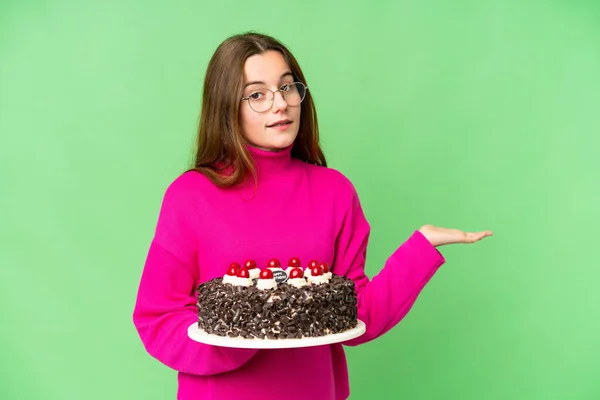 Teenager girl holding birthday cake over isolated chroma key background extending hands to the side for inviting to come