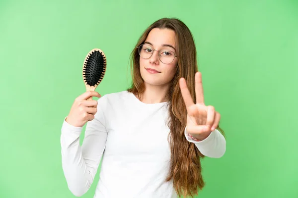 Teenager girl with hair comb over isolated chroma key background smiling and showing victory sign