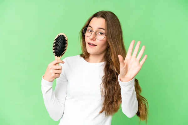 Teenager girl with hair comb over isolated chroma key background saluting with hand with happy expression