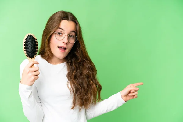 Teenager girl with hair comb over isolated chroma key background surprised and pointing finger to the side