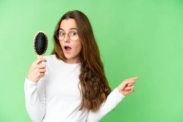 Teenager girl with hair comb over isolated chroma key background surprised and pointing side