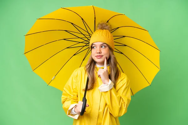 年轻姑娘穿着雨衣 披着雨伞 遮挡着孤零零的彩色背景 一边抬头 一边想办法 — 图库照片