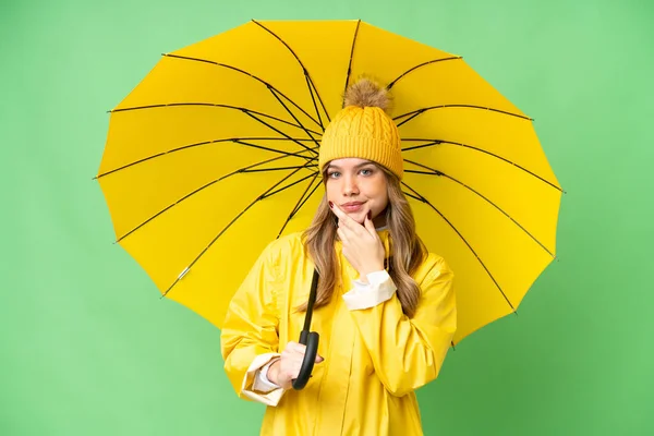 若いです女の子とともにレインプルーフコートと傘上の隔離されたクロマキー背景思考 — ストック写真