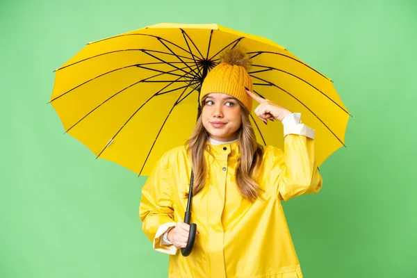 若いです女の子とともにレインプルーフコートと傘上の隔離されたクロマキー背景持っています疑問と思考 — ストック写真