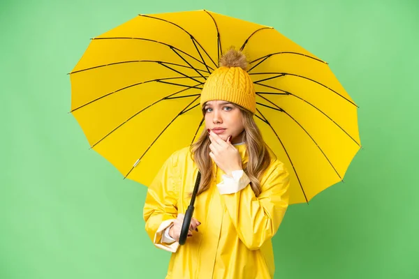 穿着防雨外套 披着雨伞 罩在孤立的彩色关键背景之上的小女孩 有着疑虑和思考 — 图库照片
