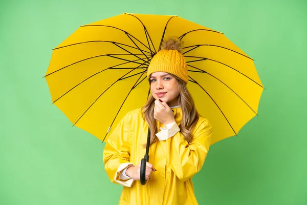 若いです女の子とともにレインプルーフコートと傘上の隔離されたクロマキー背景と見上げます — ストック写真