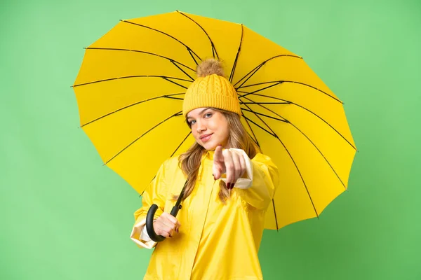 年轻姑娘穿着雨衣 披着雨伞 披着孤零零的彩色关键背景 满脸喜色地朝前看 — 图库照片