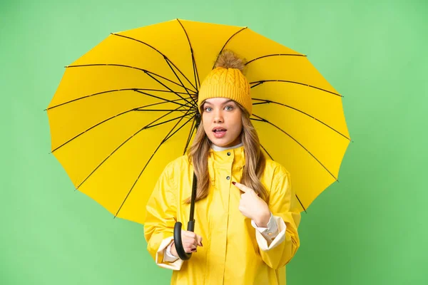 若いです女の子とともにレインプルーフコートと傘上の隔離されたクロマキー背景とともに驚きの顔の表情 — ストック写真