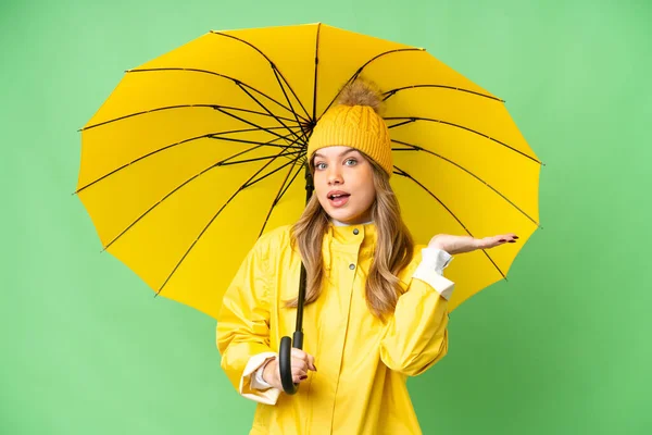 若いです女の子とともにレインプルーフコートと傘上の隔離されたクロマキー背景とともにショックを受けた顔の表情 — ストック写真