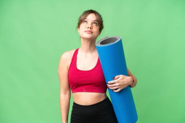 Genç sporcu kız yoga derslerine giderken elinde bir paspas tutarak izole edilmiş krom anahtar arka planına bakıyor.