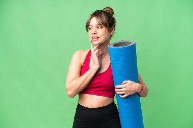 Genç sporcu kız yoga derslerine giderken izole edilmiş krom anahtar arka planında bir minder tutuyor gülümserken yukarı bakıyor.