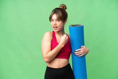 Genç sporcu kız yoga derslerine giderken elinde bir paspas tutarak izole edilmiş bir krom anahtar arka planda zaferi kutluyor.