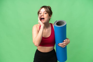 Genç sporcu kız yoga derslerine giderken izole edilmiş krom arka planda bir paspas tutuyor ve ağzı açık bağırıyor.