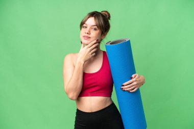 Genç spor kızı yoga derslerine giderken izole edilmiş krom anahtar arka planda elinde bir minder tutarken mutlu ve gülümsüyor.