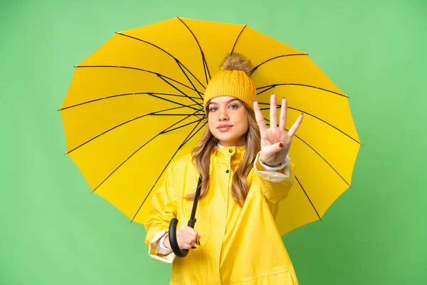 年轻姑娘穿着雨衣 披着雨伞 独立的彩色关键背景 幸福极了 她用手指数着四个 — 图库照片