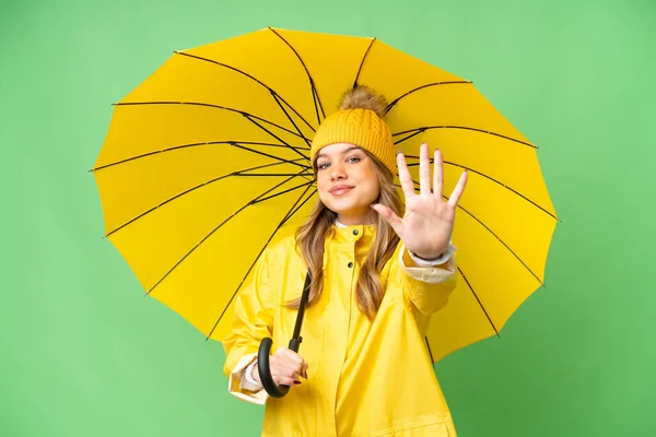 穿着防雨外套和雨伞的小女孩用手指数到5个 覆盖在孤立的彩色关键背景上 — 图库照片