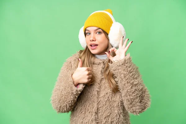 年轻姑娘披着冬衣 罩在孤立的彩色关键背景上 露出好的手势和竖起大拇指的姿势 — 图库照片