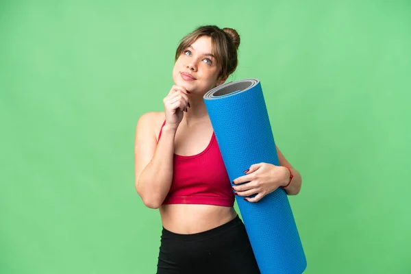 年轻的女运动员一边去上瑜伽课 一边拿着垫子盖着孤立的彩色关键背景 抬头看 — 图库照片