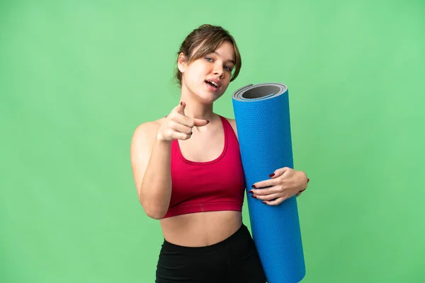 年轻的女运动员一边去上瑜伽课 一边拿着垫子盖着孤零零的彩色关键背景 带着快乐的表情指着前方 — 图库照片