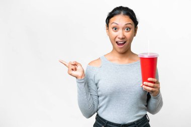Young Uruguayan woman holding soda over isolated white background surprised and pointing finger to the side