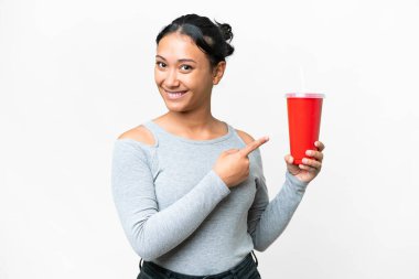 Young Uruguayan woman holding soda over isolated white background and pointing it