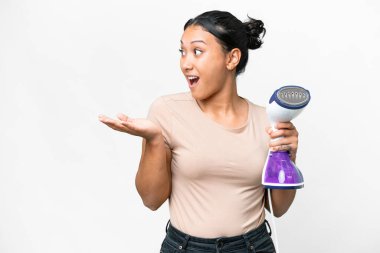 Young Uruguayan woman holding a vertical steam iron over isolated white background with surprise facial expression