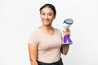 Young Uruguayan woman holding a vertical steam iron over isolated white background smiling a lot