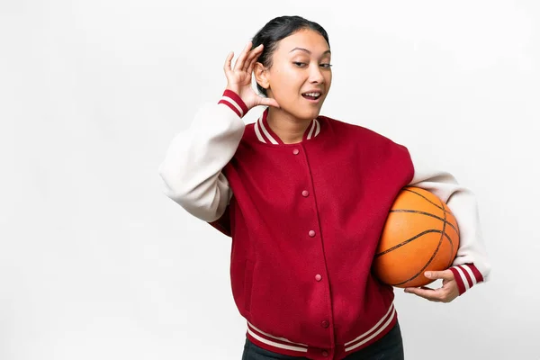 若いですウルグアイ女性プレイバスケットボール上の隔離された白い背景上に何かを聞いて耳に手を置くことによって — ストック写真