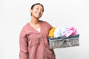 Young Uruguayan woman holding a clothes basket over isolated white background laughing