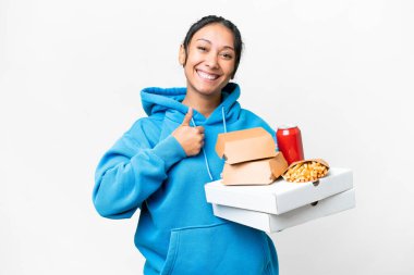 Young Uruguayan woman holding pizzas and burgers over isolated white background giving a thumbs up gesture