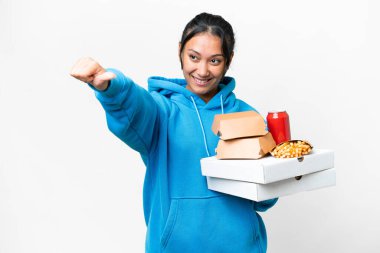 Young Uruguayan woman holding pizzas and burgers over isolated white background giving a thumbs up gesture