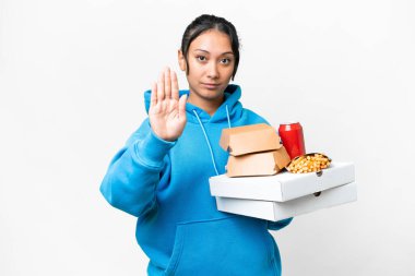 İzole edilmiş beyaz arka planda pizza ve hamburger tutan genç Uruguaylı kadın dur hareketi yapıyor.