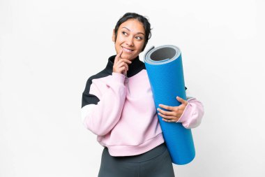 Young sport woman going to yoga classes while holding a mat over isolated white background thinking an idea while looking up