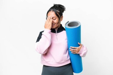 Genç sporcu kadın yoga derslerine giderken beyaz arka planda bir paspas tutuyor ve gülüyor.
