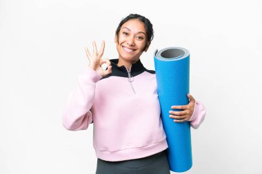 Genç sporcu kadın yoga derslerine giderken elinde paspas tutarken parmaklarıyla işaret dilini gösteriyor.