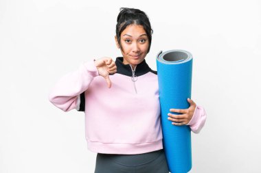 Genç sporcu kadın yoga derslerine gidiyor. Elinde paspas, izole edilmiş beyaz arka planda. Başparmağında negatif ifade var.