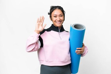 Genç sporcu kadın yoga derslerine gidiyor. Elinde paspas, izole edilmiş beyaz arka planda. Mutlu bir ifadeyle selam veriyor.