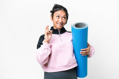 Young sport woman going to yoga classes while holding a mat over isolated white background with fingers crossing and wishing the best