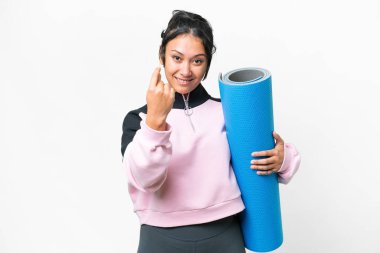 Genç sporcu kadın yoga derslerine gidiyor. Elinde paspas, beyaz arka planda. Gelen hareketi yapıyor.