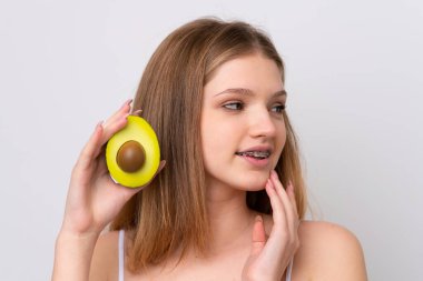 Genç Rus kız beyaz arka planda izole edilmiş, elinde avakado tutarken gülümsüyor. Portreyi kapat