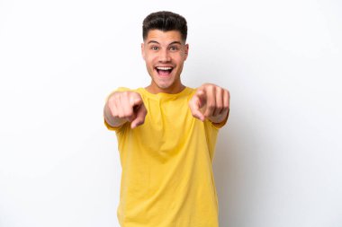 Beyaz arka planda izole edilmiş genç beyaz adam şaşırmış ve ön tarafı işaret ediyor.