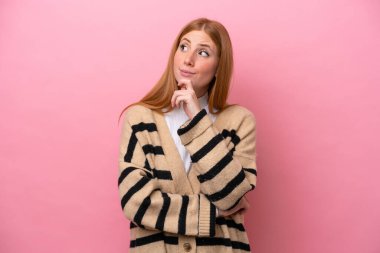 Genç kızıl saçlı kadın pembe arka planda izole edilmiş ve yukarı bakıyor.