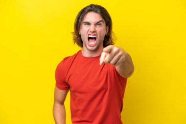 Beyaz tenli yakışıklı adam sarı arka planda izole edilmiş hayal kırıklığına uğramış ve ön tarafı işaret ediyor.