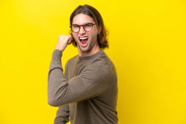 Caucasian handsome man isolated on yellow background celebrating a victory