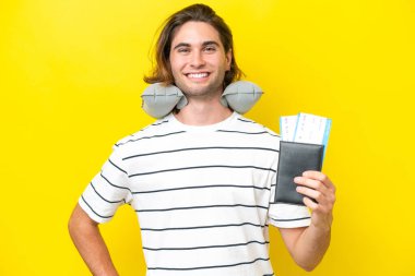 Şişirilebilir seyahat yastığı olan yakışıklı adam kolları kalçasında ve gülümsüyor.