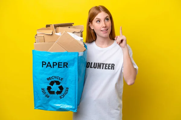Młoda Ruda Kobieta Trzyma Torbę Pełną Papieru Recyklingu Odizolowaną Żółtym — Zdjęcie stockowe