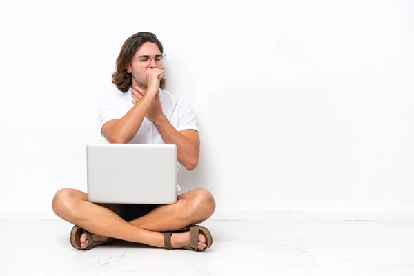 Young handsome man with a laptop sitting on the floor isolated on white background is suffering with cough and feeling bad