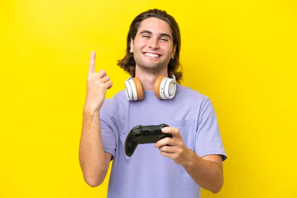 若いですハンサムなCaucasian男遊びますとともにビデオゲームコントローラ上の隔離された上に黄色の背景に素晴らしいアイデアを指して — ストック写真
